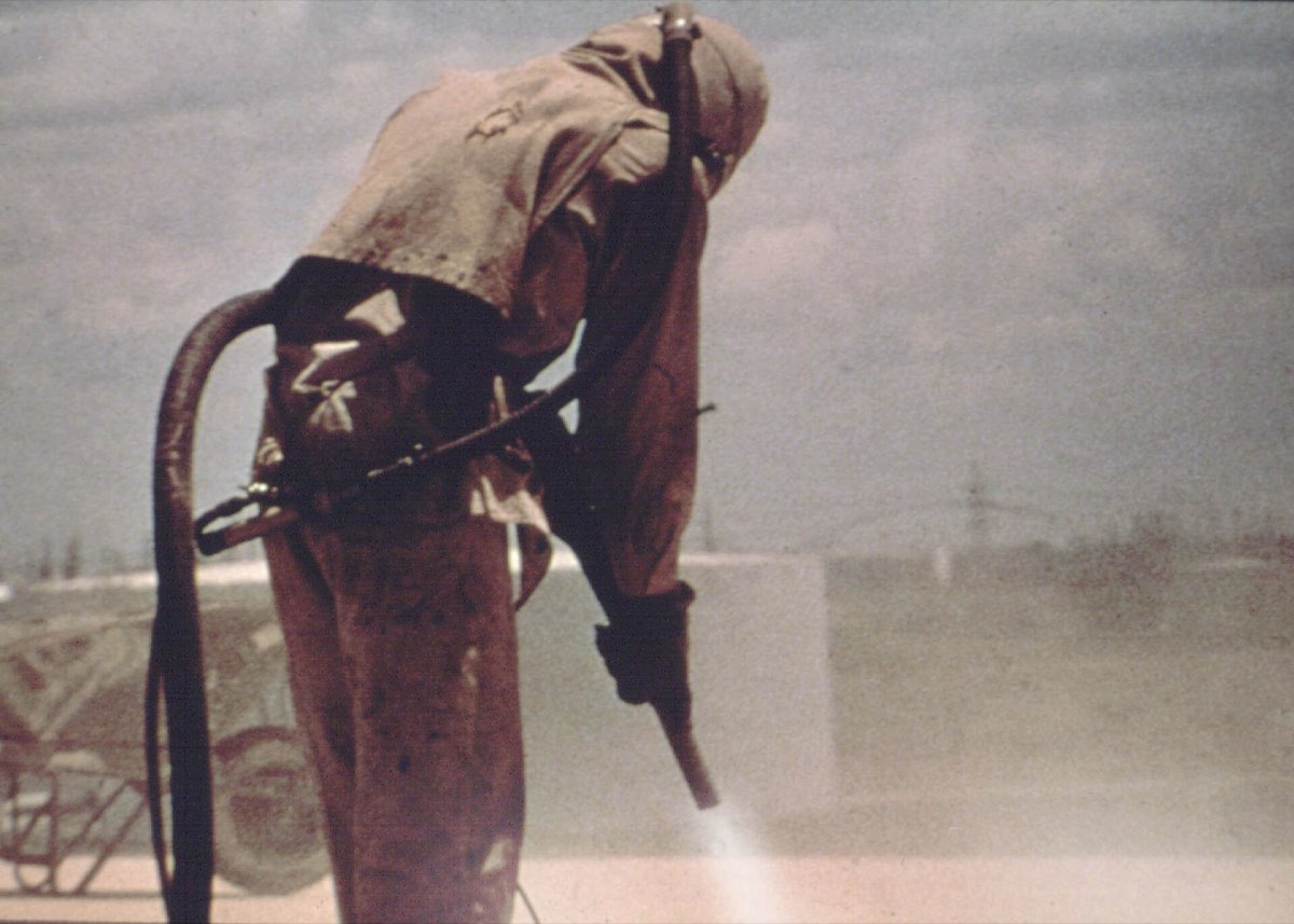 Worker in full protective gear abrasive-blasting a surface