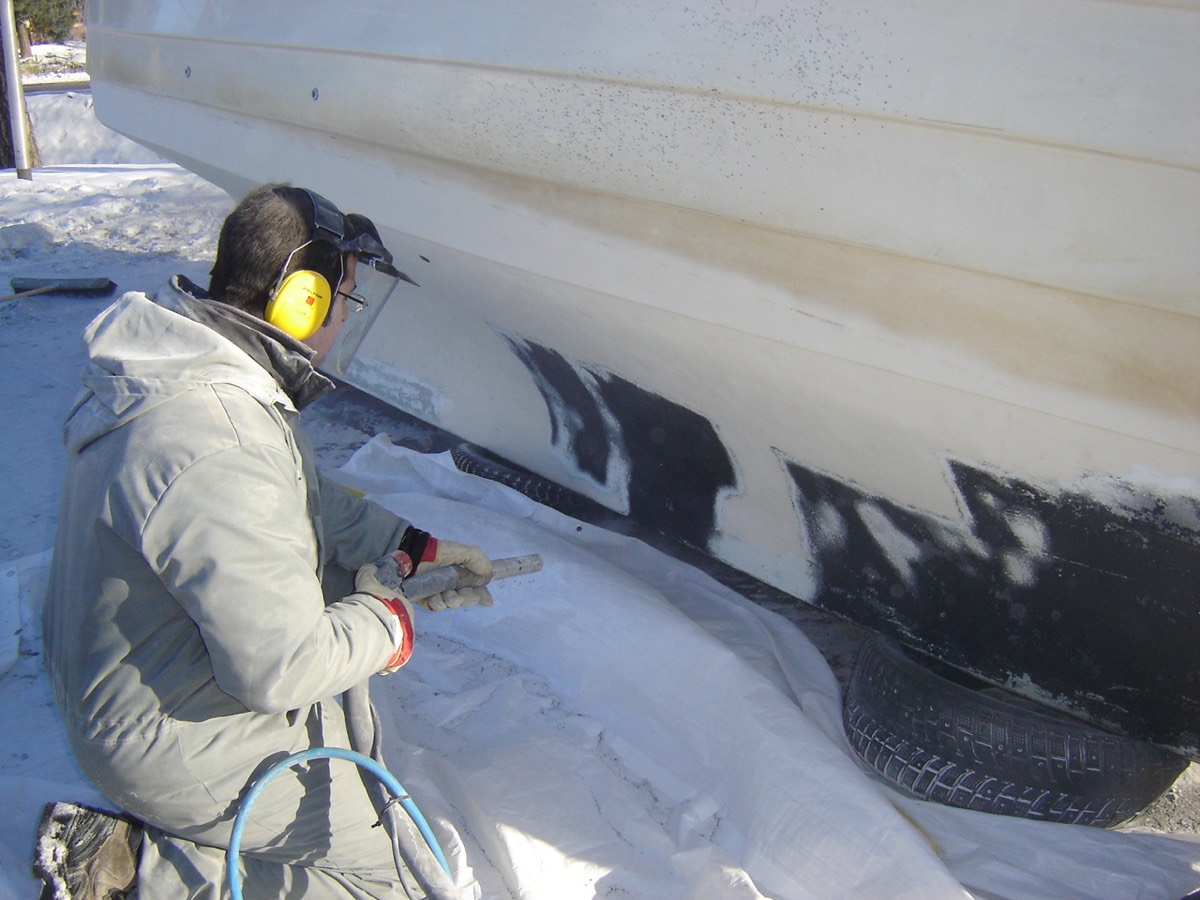 Worker in protective gear blast-cleaning a hull